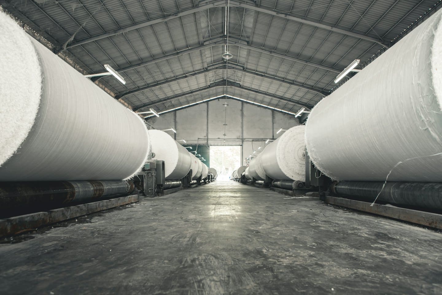 Grandi rotoli di materiale bianco si muovono attraverso macchinari industriali di fabbrica.